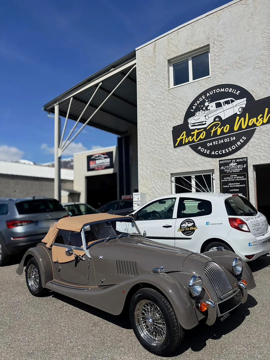 Photo retouchée : la façade du centre Auto Pro Wash à Gap avec son enseigne, un roadster et la voiture de service devant l'atelier